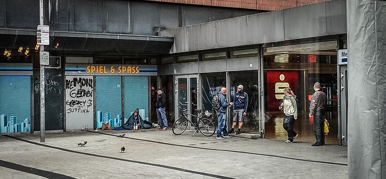 Das Foto zeigt einen Obdachlosen am Hauptbahnhof Hannover. Er sitzt vor einer ehemaligen Spielhalle. Eine Reklame über ihm lautet Spiel und Spass. Es ist ein trauriger Anblick an diesem Sonntag morgen.