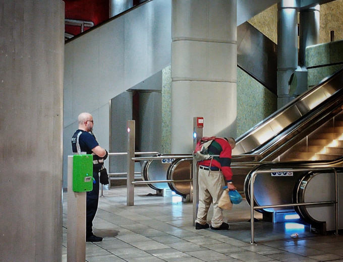 Das Bild zeigt den U-Bahnhof Kröpcke in Hannover. Von einem bulligen ''Sicherheits''mann der Firma Protec, breitbeinig, mit verschränkten Armen, genau beobachtet, muß ein Obdachloser, ein gebrechlicher, klappriger alter Mann, den Bahnhof verlassen. Rauswurf. Der alte Mann schafft es kaum die Rolltreppe hoch.